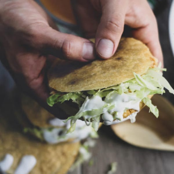 Hands holding a Mexican gordita filled with meat, lettuce, and white sauce.