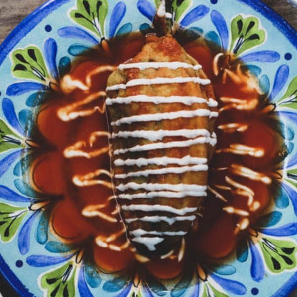 A chile relleno, drizzled with crema, sits in a pool of red sauce on a colorful plate.