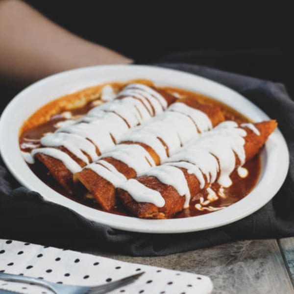 Three enchiladas covered in red sauce and drizzled with white crema, served on a white plate.