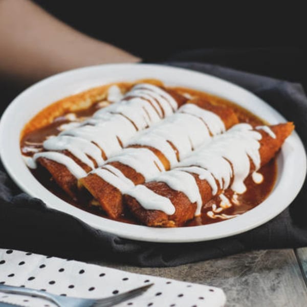 Three enchiladas covered in red sauce and drizzled with white cream, served on a white plate.