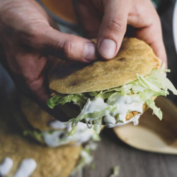Hands holding a Taqueria Cuernavaca gordita filled with meat, lettuce, and white sauce.