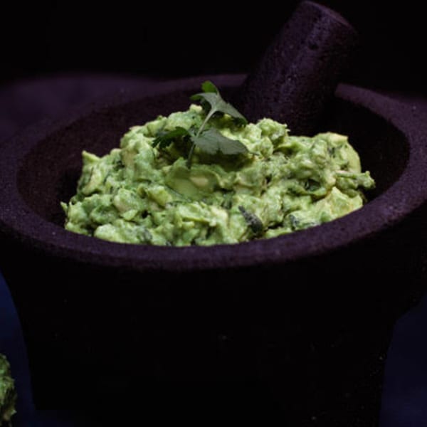 Freshly made guacamole with cilantro in a dark molcajete, ready to be served.