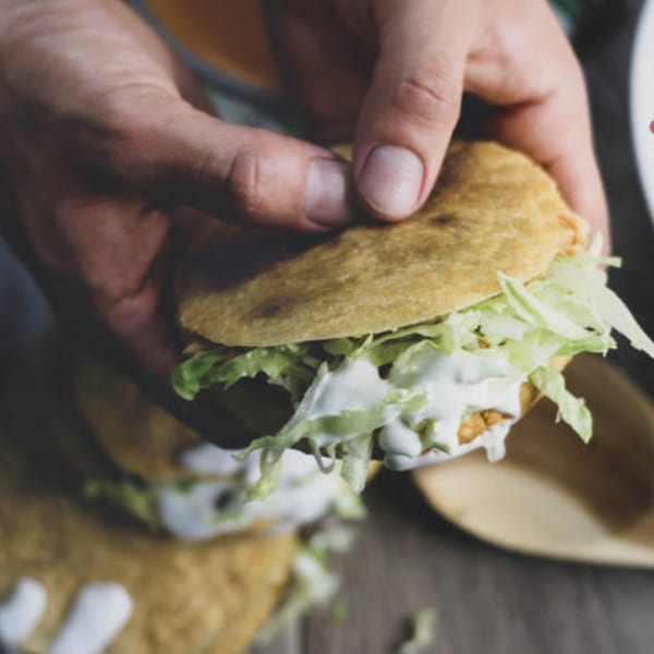 Hands holding a Mexican gordita filled with shredded lettuce and white cream sauce.