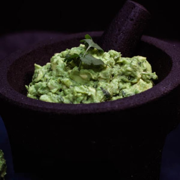 Freshly made guacamole, garnished with cilantro, in a dark stone molcajete.