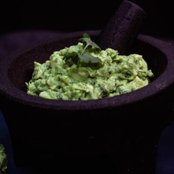 Fresh guacamole with cilantro in a dark molcajete, ready to be served.
