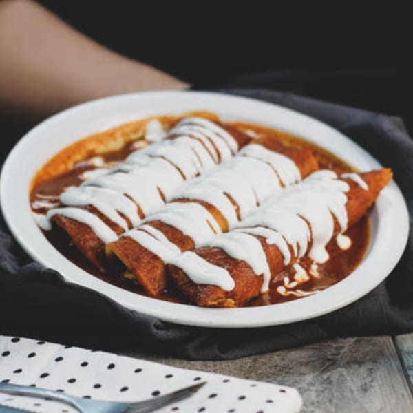 Three enchiladas covered in red sauce and drizzled with white cream, served on a white plate.