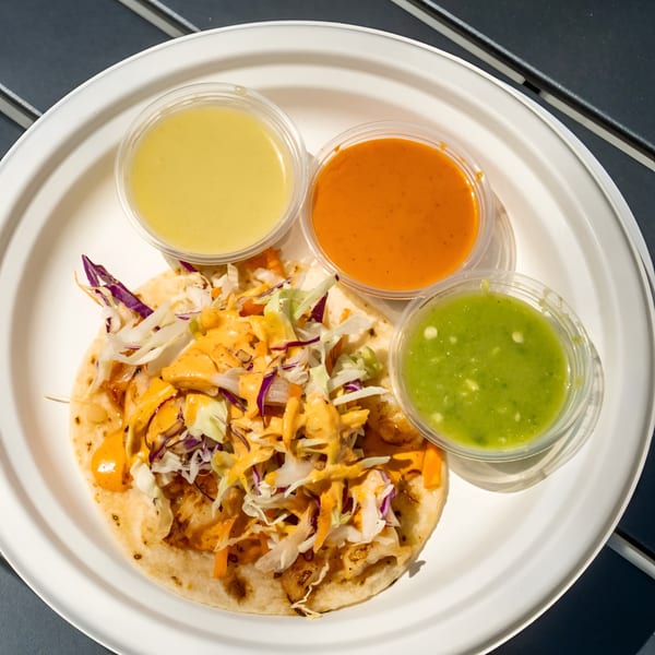 Taqueria Cuernavaca taco with cabbage, sauce, and three sides of salsa on a white plate.