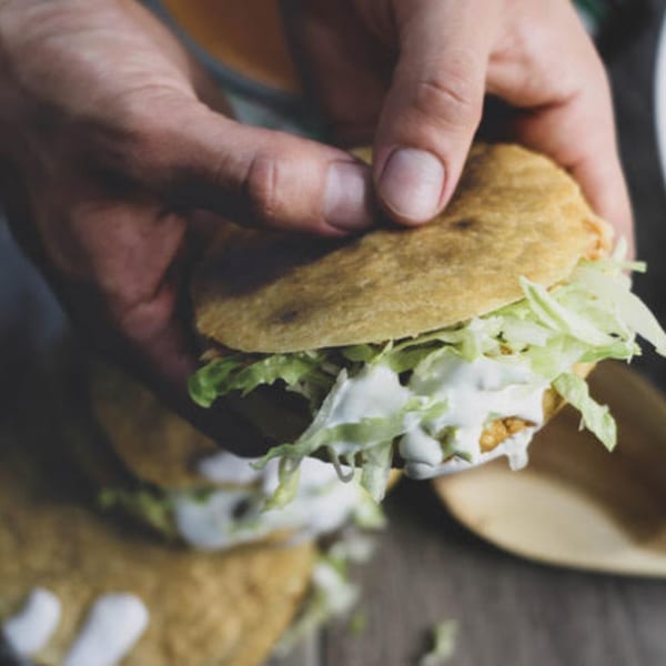 Hands holding a Mexican gordita filled with shredded lettuce and white cream sauce.