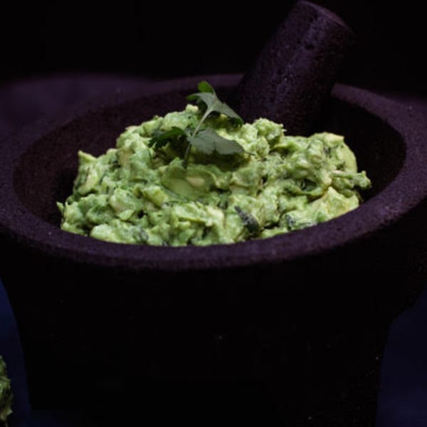 Freshly made guacamole with cilantro in a dark molcajete, ready to be served.