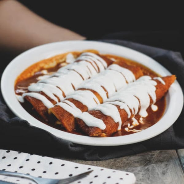 Three enchiladas covered in red sauce and drizzled with white crema, served on a white plate.