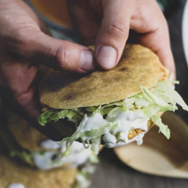Hands holding a Mexican gordita filled with shredded lettuce and white cream sauce.